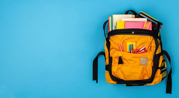 sac d'école jaune plein de livres sur fond bleu - Photo, image