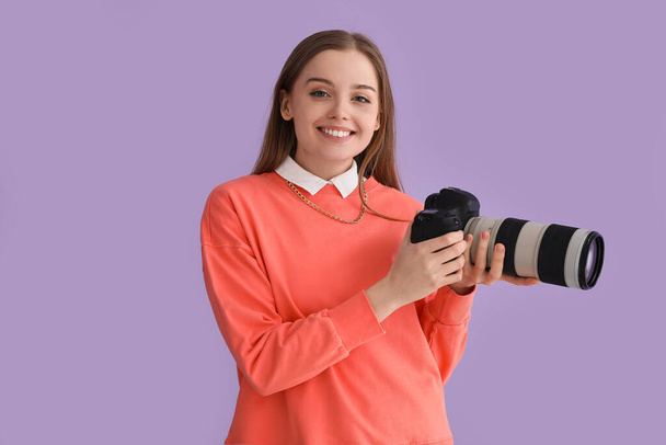 Joven fotógrafa con cámara profesional sobre fondo lila - Foto, imagen