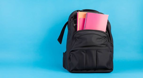 маленька чорна шкільна сумка, повна книг на синьому фоні HD - Фото, зображення