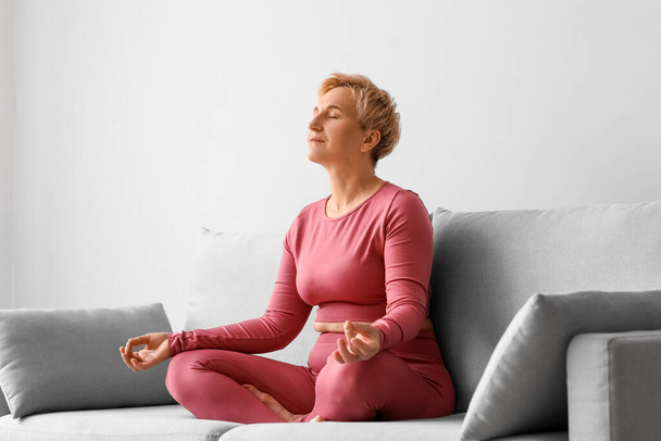 Mujer madura meditando mientras está sentado en el sofá - Foto, imagen