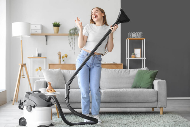 Young woman with vacuum cleaner singing at home - Fotoğraf, Görsel