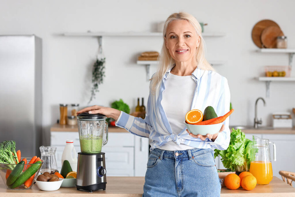 Зріла жінка робить здорову смужку з блендером на кухні - Фото, зображення