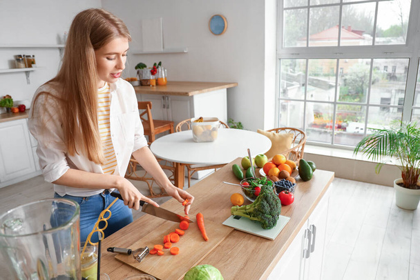 Giovane donna taglio carota in cucina - Foto, immagini