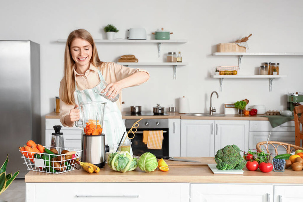 Young woman pouring water into blender with healthy food in kitchen - Photo, Image