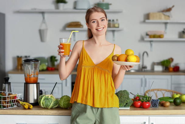Mutfakta bir bardak sağlıklı meyve suyu ve meyve suyu olan genç bir kadın. - Fotoğraf, Görsel