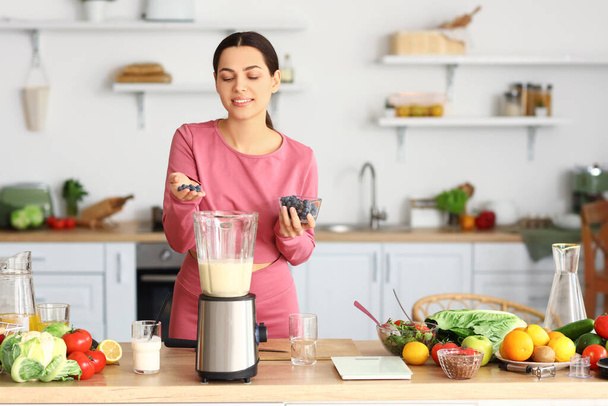 Urheilullinen nuori nainen tekee terveellistä smoothie mustikoilla keittiössä - Valokuva, kuva