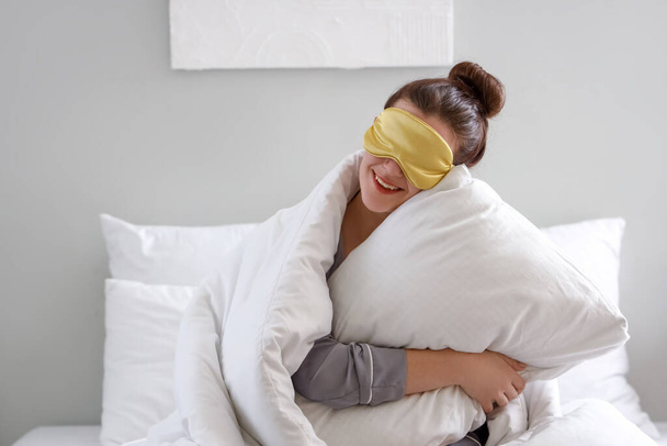 Πρωί της νεαρής γυναίκας με μάσκα ύπνου και μαξιλάρι στην κρεβατοκάμαρα - Φωτογραφία, εικόνα