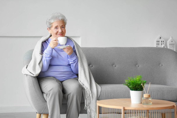 Mujer mayor con cuadros bebiendo café en el sofá en casa - Foto, Imagen
