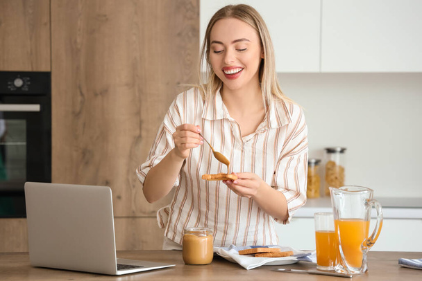 Young woman spreading tasty nut butter onto toast in kitchen - Photo, Image