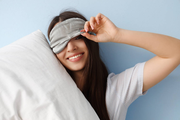 Молодая женщина в маске для сна с подушкой на синем фоне, крупным планом - Фото, изображение
