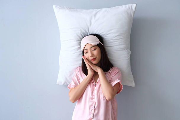 Schöne Asiatin im Schlafanzug mit Kissen auf grauem Hintergrund - Foto, Bild