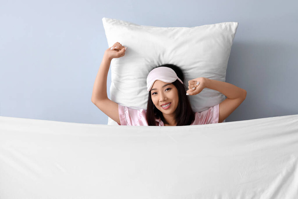 Schöne asiatische Frau mit Kissen und Decke auf grauem Hintergrund - Foto, Bild