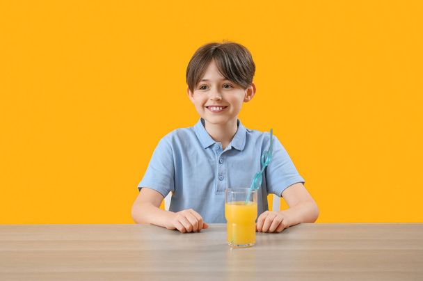 カラーバックグラウンドのテーブルにオレンジジュースのガラスを持つ小さな少年 - 写真・画像