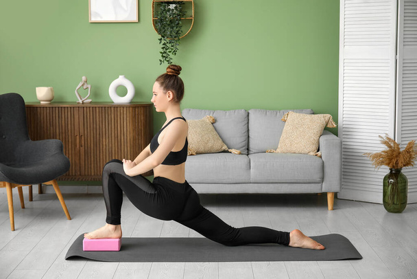 Sporty young woman practicing yoga with block at home - Photo, Image