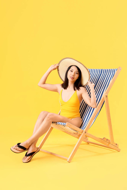 Красивая азиатка расслабляется в шезлонге на желтом фоне - Фото, изображение