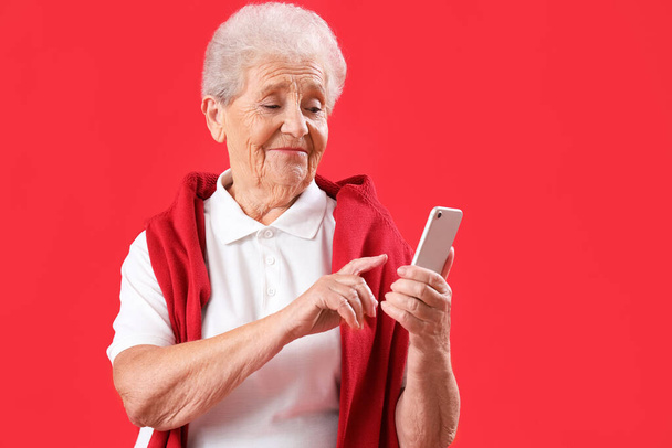Mujer mayor usando teléfono móvil sobre fondo rojo - Foto, imagen