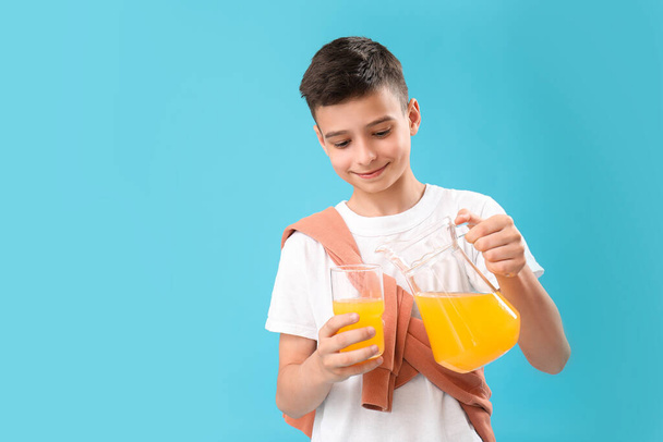 青い背景にガラスにオレンジジュースを注ぐ小さな少年 - 写真・画像