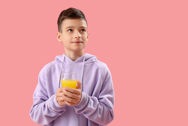 Pembe arka planda bir bardak portakal suyu olan küçük çocuk. - Fotoğraf, Görsel
