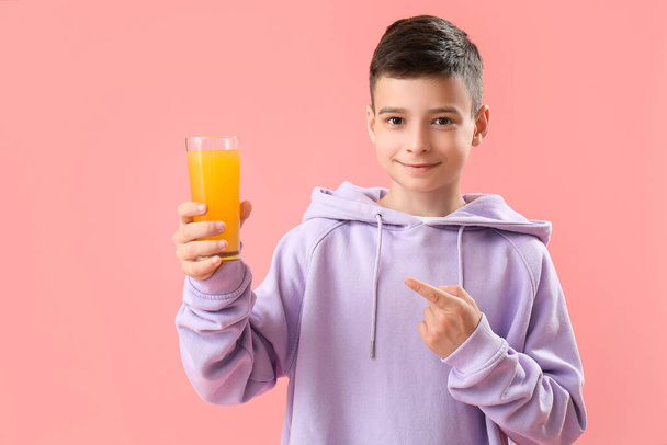 ピンクの背景にあるオレンジジュースのガラスを指す小さな少年 - 写真・画像