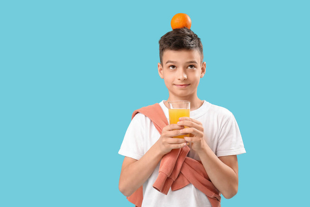 Mały chłopiec ze szklanką soku i pomarańczą na niebieskim tle - Zdjęcie, obraz