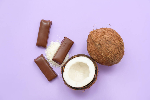 Lekkere chocolade bedekt snoepjes en kokosnoten op lila achtergrond - Foto, afbeelding