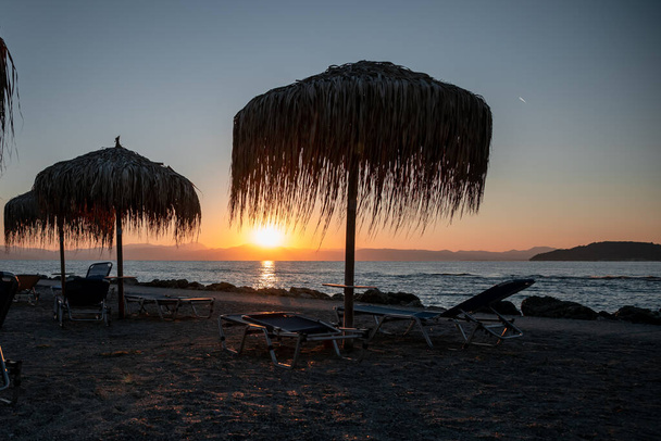 Manhã no resort: raios de sol rompendo as folhas de palma no guarda-chuva da praia. Silhuetas de cadeiras de praia, guarda-chuvas e o cais visível à distância. Foto de alta qualidade - Foto, Imagem
