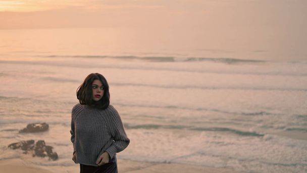 Lonely romantic girl enjoy cloudy seascape standing alone near calm ocean waves. Attractive young woman wearing gray sweater standing on gloomy seashore. Serious model posing on nature evening time. - Foto, imagen