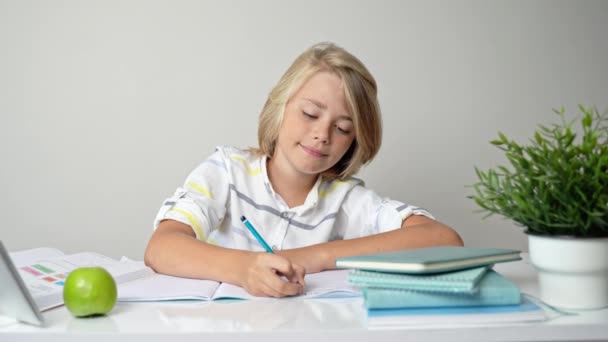 Estudiante sonriente de la escuela secundaria sentado en el escritorio, estudiando escritura de libros y tableta en casa de la clase Volver a la escuela. Infancia, educación para los niños - Metraje, vídeo