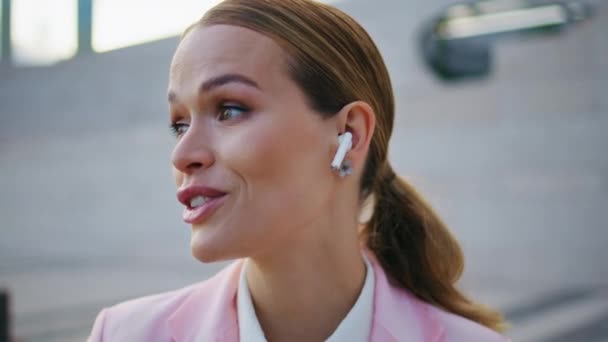 Woman wearing earbuds talking sitting urban area close up. Portrait of glamorous business lady in earphones have work conversation outdoors. Elegant girl manager solving tasks by remote communication. - Footage, Video