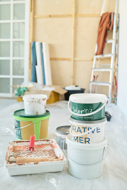 Dvě hromádky plastových kbelíků s barvami na stěny a malířem v podnosu stojícím na podlaze obývacího pokoje v novém bytě - Fotografie, Obrázek