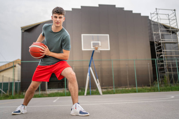 Um adolescente caucasiano homem jovem caucasiano ficar na quadra de basquete com bola à noite pronto para jogar jogo cópia espaço pessoa real - Foto, Imagem