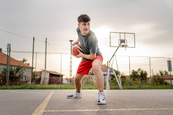 Een tiener Kaukasische mannelijke Kaukasische jongeman staan op basketbalveld met bal in de avond klaar om spel kopiëren ruimte echte persoon spelen - Foto, afbeelding