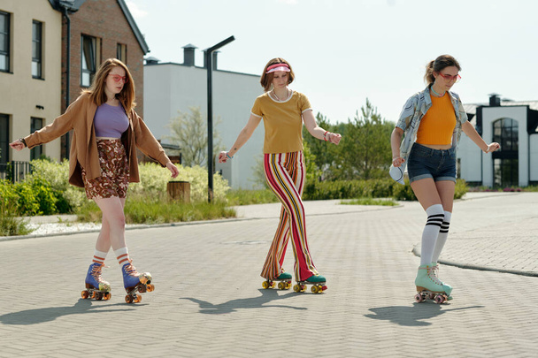 Три активні дівчата-підлітки в повсякденному одязі катаються на роликах у міському середовищі і насолоджуються дозвіллям у сонячний літній день або вихідні - Фото, зображення