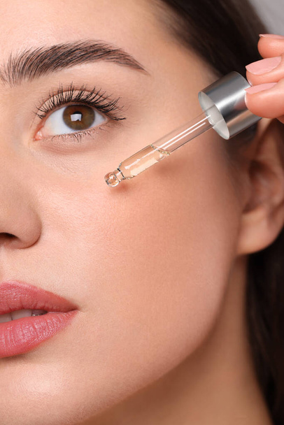 Young woman applying essential oil onto face, closeup - Фото, зображення