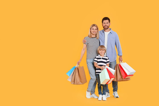 Family shopping. Happy parents and son with paper bags on orange background. Space for text - Foto, Bild