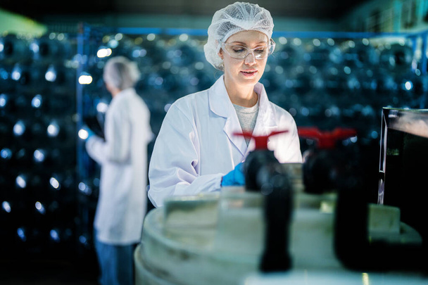 Працівник заводу перевіряє пляшки води на складі на промисловому заводі. Жінка-працівник фіксує дані на виробництві напоїв лінії. - Фото, зображення