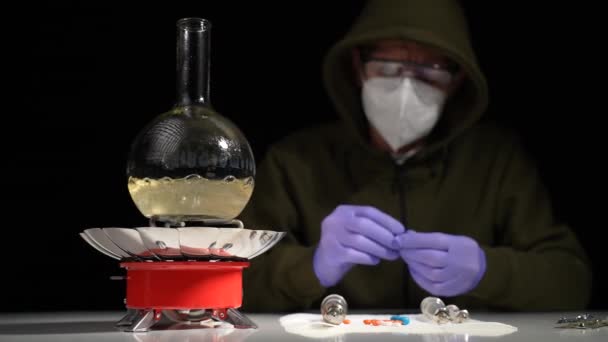 Un químico en un laboratorio subterráneo cocina una droga en un frasco de vidrio en un quemador de gas - Imágenes, Vídeo