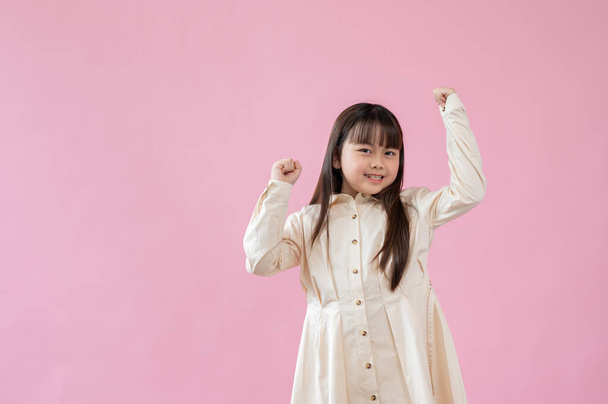 Una niña asiática alegre y linda de pie con las manos en alto, sonriendo a la cámara, de pie sobre un fondo rosa aislado. - Foto, Imagen