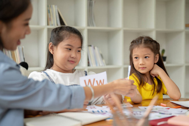 Kaksi suloista aasialaista tyttöä keskittyy opiskelemaan englantilaisia aakkosia taskukortteja yksityisen opettajan kanssa kotona. esikoulu, päiväkoti, peruskoulu - Valokuva, kuva