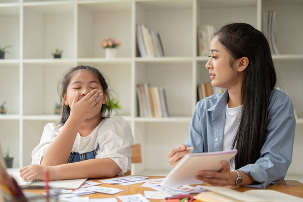 Eine schöne und freundliche asiatische Lehrerin oder Privatlehrerin redet und überzeugt ein schläfriges, faules Mädchen, zu lernen und auf eine Lektion zu achten. - Foto, Bild