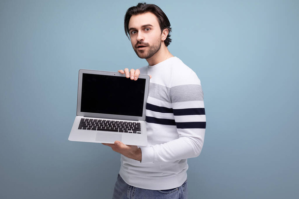 όμορφος καυκάσιος μελαχρινός νεαρός άνδρας που δείχνει οθόνη laptop για να εισάγει προωθητική προσφορά. - Φωτογραφία, εικόνα
