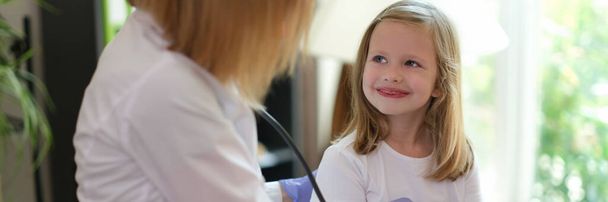Young female patient smiles at doctor at medical examination. Nurse listens to heartbeat of happy girl in medical clinic. - Foto, Bild