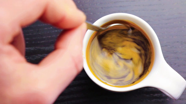 Cup of coffee with adult hand that use a spoon inside, on black wood table - Filmmaterial, Video