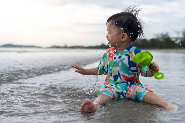 Onnellinen 1-2-vuotias lapsi nauttii leikkimisestä rannalla roiskeella lämpimällä merivedellä - Valokuva, kuva
