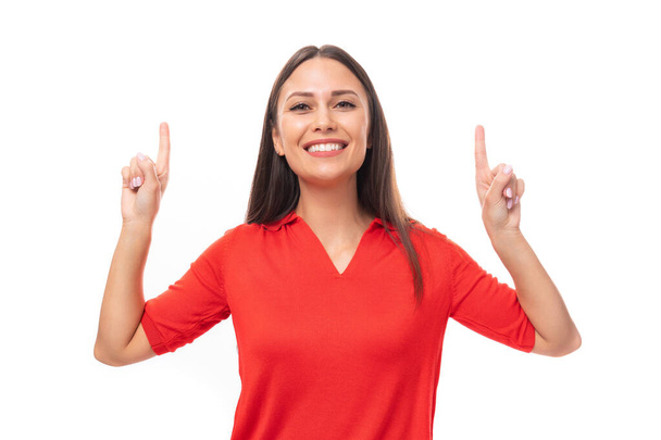 verrast brunette vrouw in een rode stijlvolle v-hals blouse toont haar hand naar de lege ruimte. - Foto, afbeelding