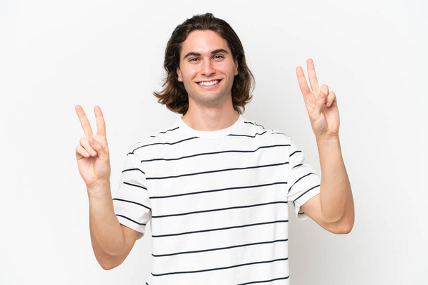 Молодой красивый мужчина на белом фоне показывает знак победы обеими руками - Фото, изображение