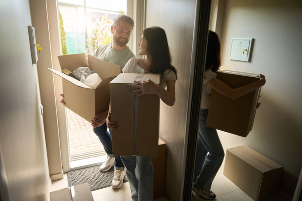 Smiling man and woman looking at each other while bringing boxes into home - Foto, imagen