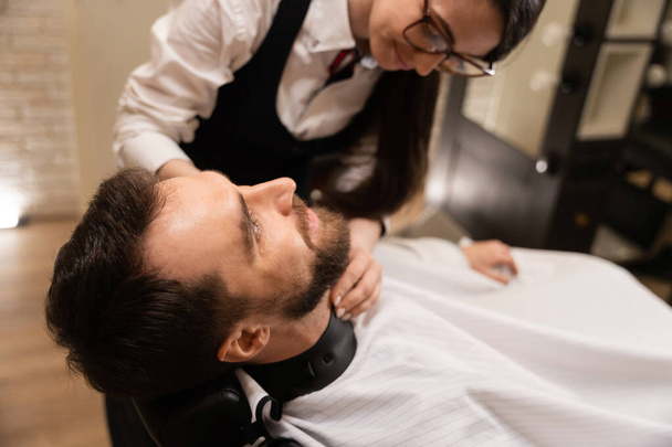 Homme dans un salon de coiffure se coupant la barbe, le maître utilise des outils spéciaux - Photo, image