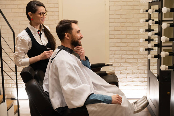 Мужчина в парикмахерской общается с хозяином, у женщины в руках клипер - Фото, изображение