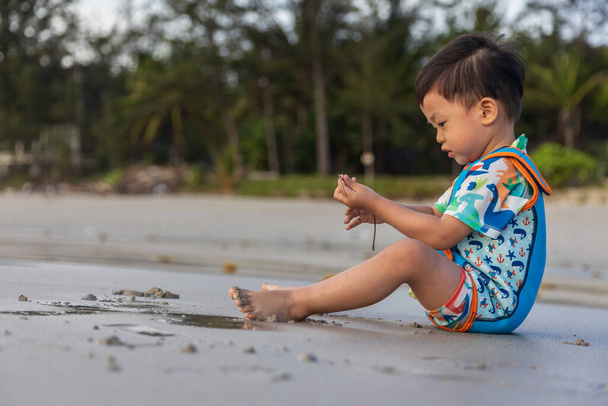 Niño chino asiático feliz jugando en la playa. El chico se divierte al aire libre. Vacaciones de verano y concepto de estilo de vida saludable - Foto, imagen